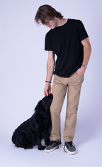 Man wearing khaki Fletch performance 5-pocket pants with a black T-shirt beside a black dog